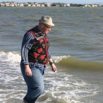 Photo: Guy in poinsettia ugly Christmas sweater vest strolls on beach