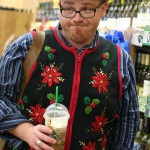 Guy in poinsettia ugly Christmas sweater vest and latte shopping at Trader Joe's